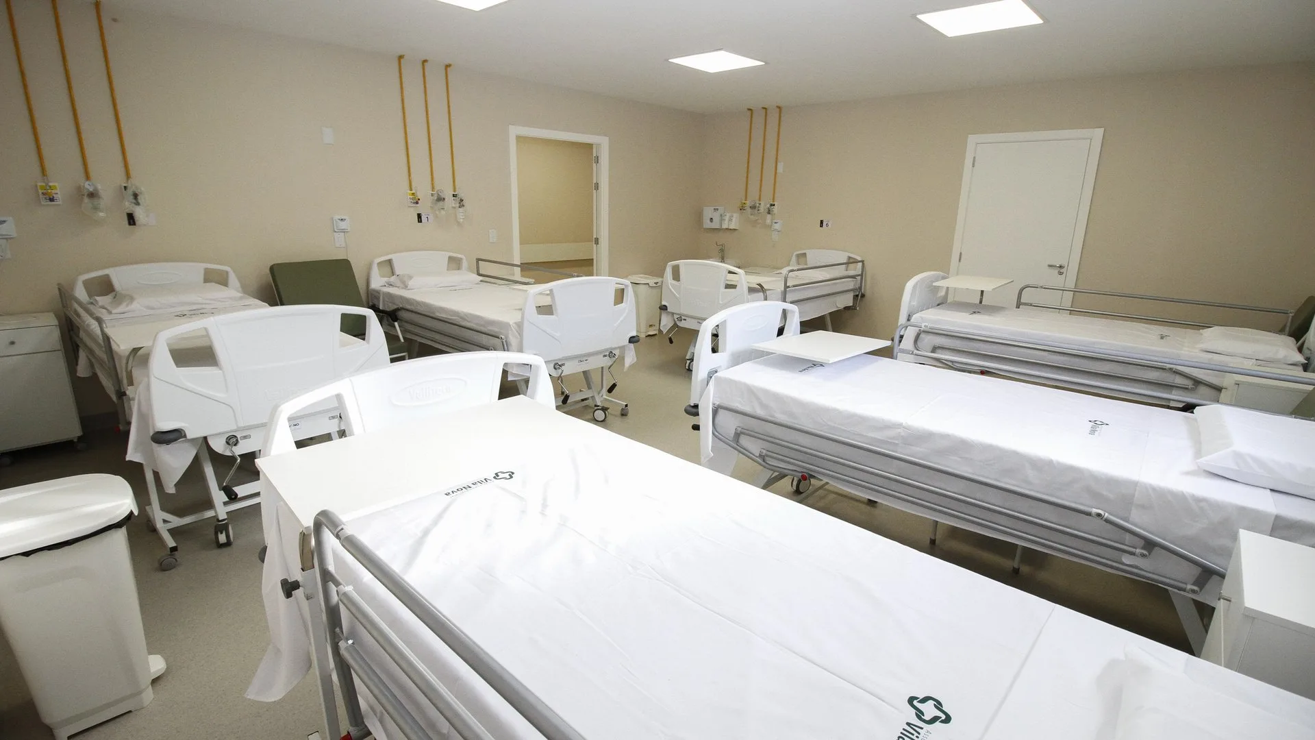 Enfermaria hospitalar com camas novas forradas de branco, réguas de gases medicinais na parede e luz natural, no Hospital Vila Nova, em Porto Alegre.